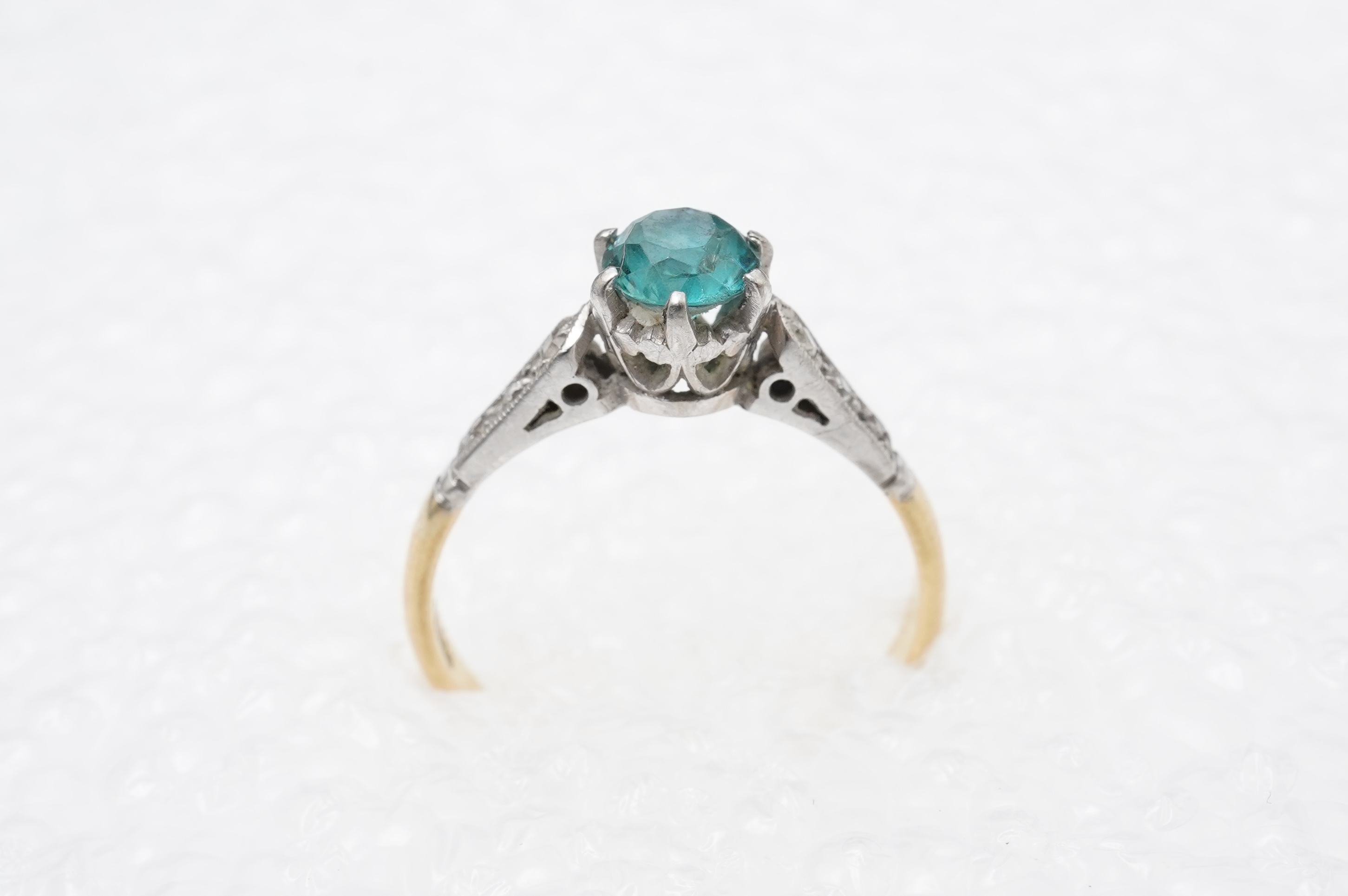 A zircon and diamond ring, mid 20th century, claw-set with a brilliant-cut blue zircon measuring approximately 5mm diameter, to shoulders set with rose-cut diamonds, mounted in gold, size N, stamped 18CT, gross weight ap